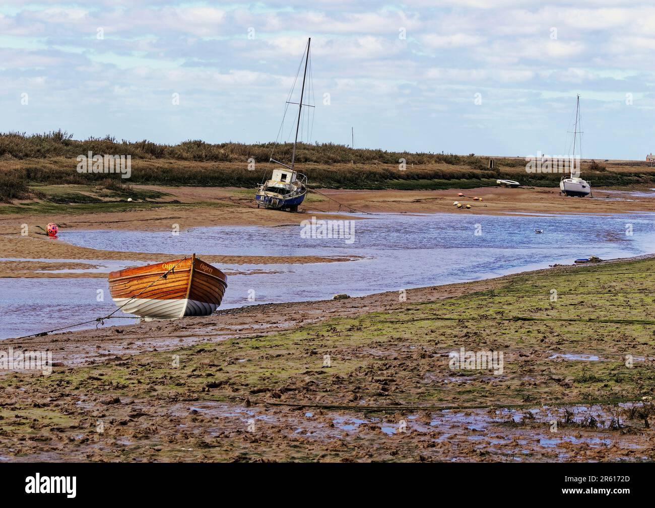 Bassa marea lungo New Cut a Blakeney, North Norfolk, con le barche lasciate in piedi sul fango in attesa della successiva marea di alluvione. Foto Stock