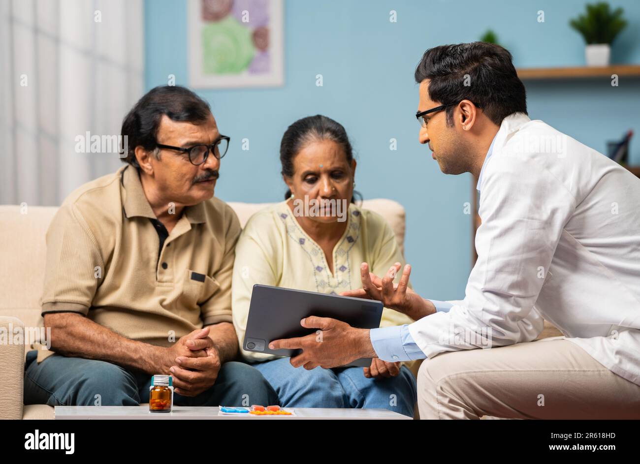 Medico indiano che spiega dal tablet digitale alla coppia anziana sul rapporto medico a casa - concetto di tecnologia, assistenza sanitaria e casa Foto Stock