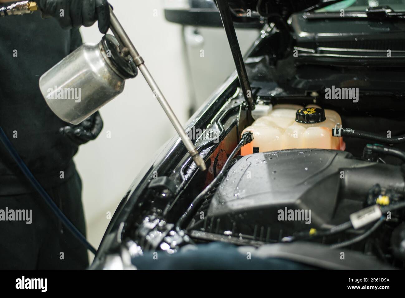 Un operatore che indossa guanti protettivi sta spruzzando un motore di automobile con una lattina di soluzione detergente Foto Stock