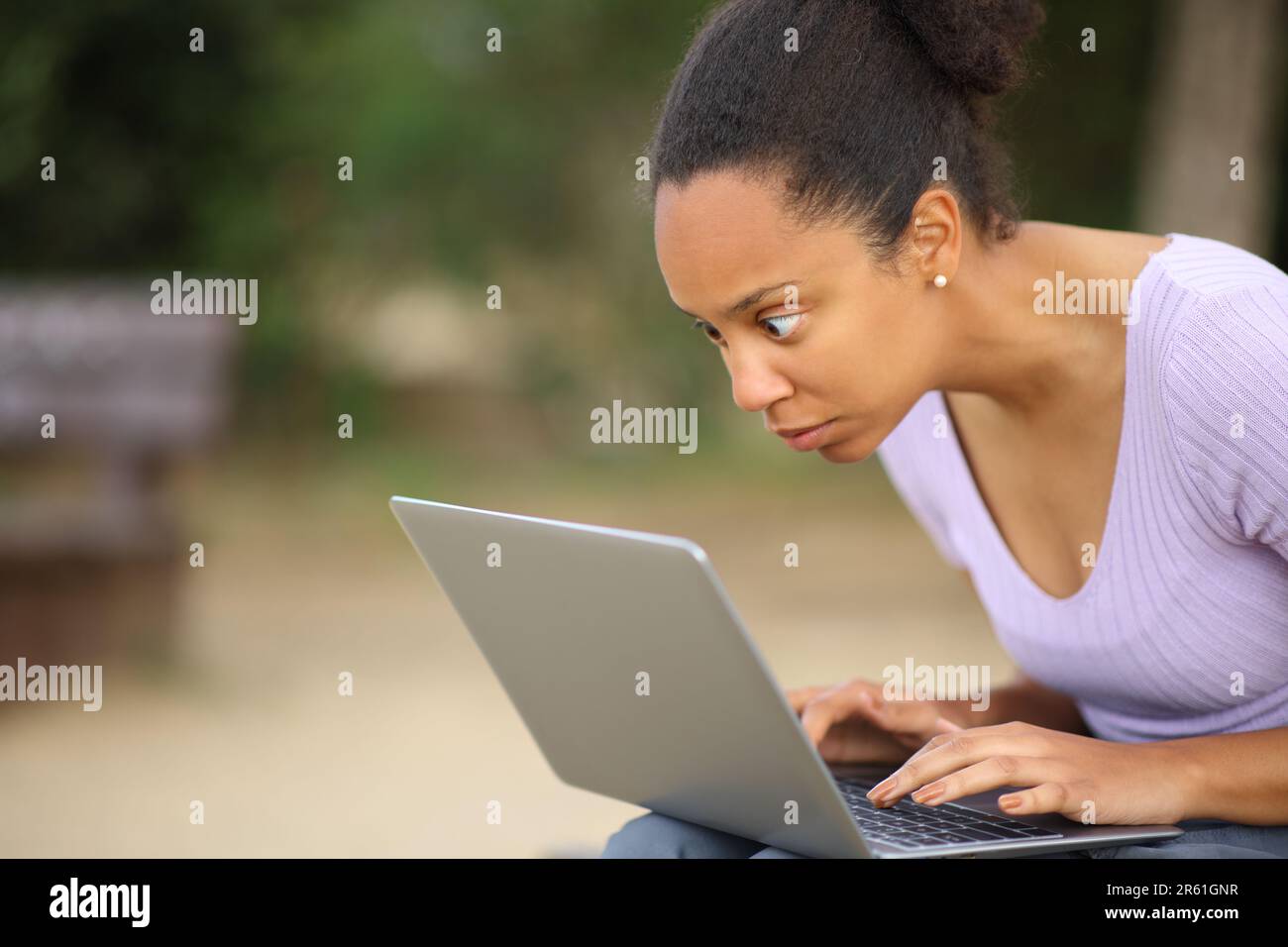 Donna nera scioccata che controlla il contenuto del notebook seduto in un parco Foto Stock