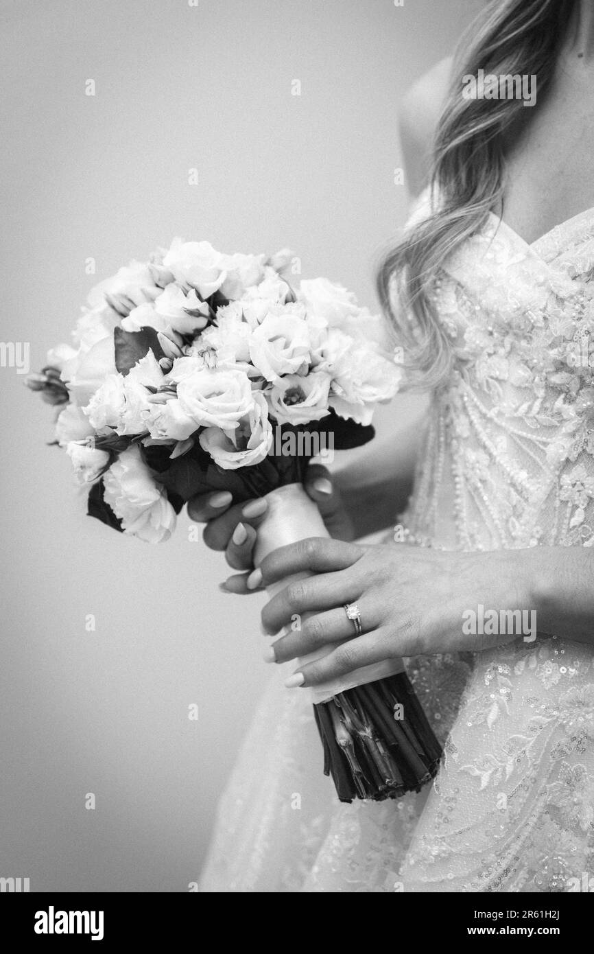 Una bella scala di grigi di una sposa, indossando un abito bianco e tenendo un bouquet di fiori bianchi Foto Stock