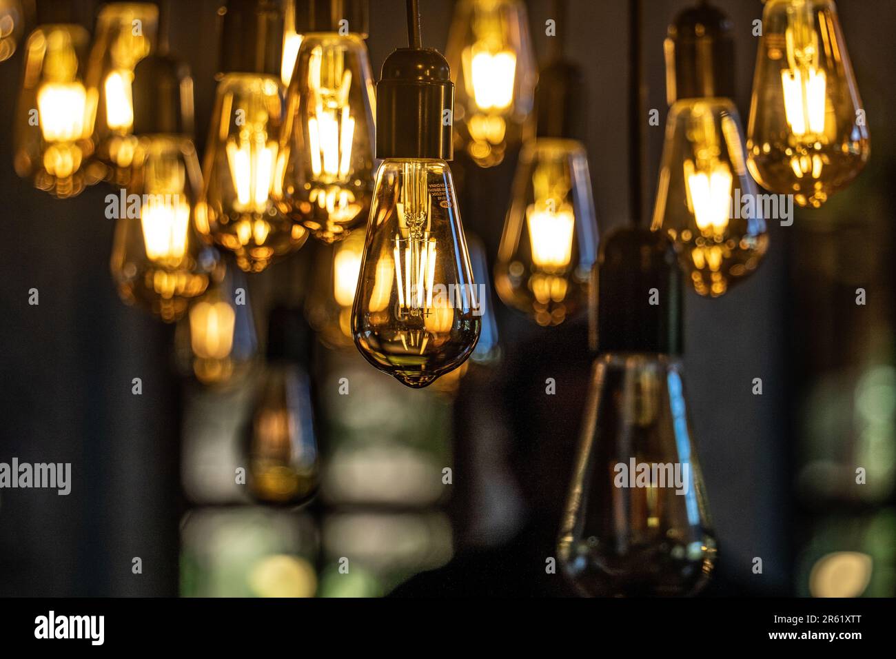 Un primo piano di una serie di lampadine illuminate sospese da un palo di metallo in una stanza poco illuminata Foto Stock