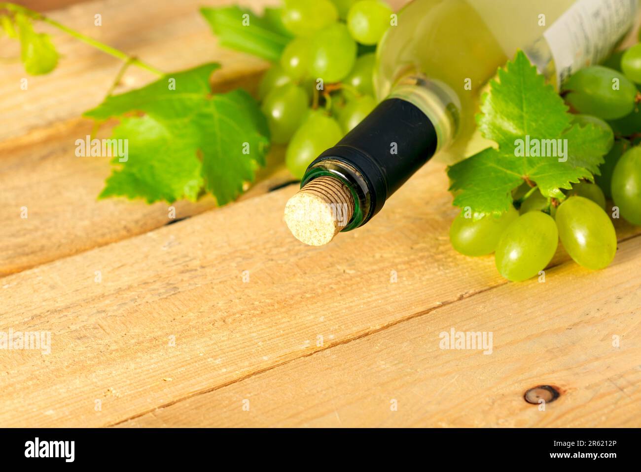 Bottiglia di vino bianco, uva e foglie su tavola di legno Foto Stock