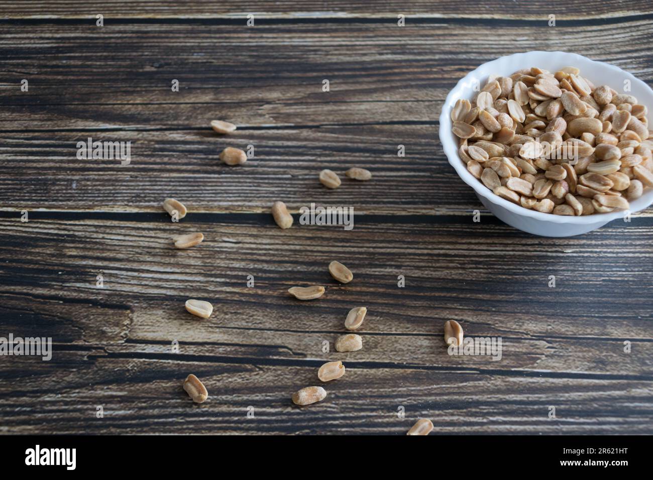 Una ciotola di ceramica bianca piena di arachidi, seduta su un tavolo di legno Foto Stock