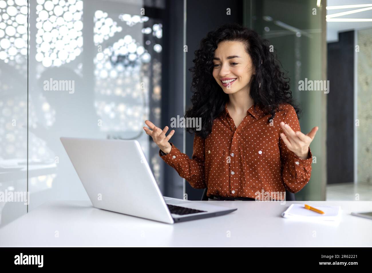 Donna d'affari ispanica felice che lavora in un ufficio moderno utilizzando un computer portatile per videochiamare e riunioni online con colleghi dipendenti, donna sorridente e divertente dando una presentazione. Foto Stock