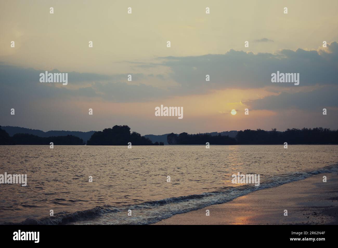Un oceano tranquillo che riflette le calde tonalità arancio e rosa del sole al tramonto, con alcune nuvole soffici nel cielo Foto Stock