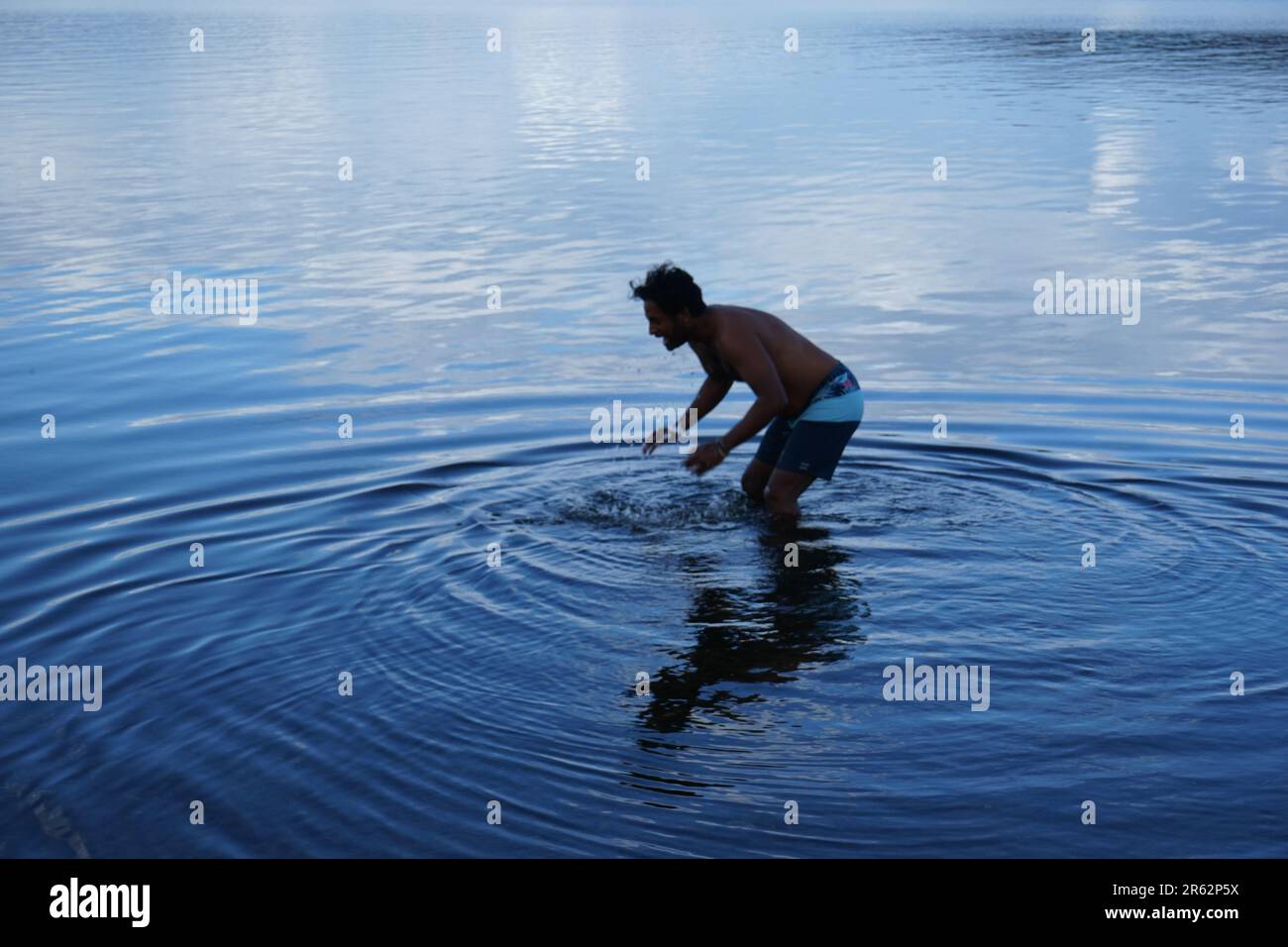 Una serena vista sul lago con acque cristalline e fredde. Un uomo si erge sul lago, creando ondulazioni circolari, abbracciando la bellezza dei dintorni remoti. Foto Stock