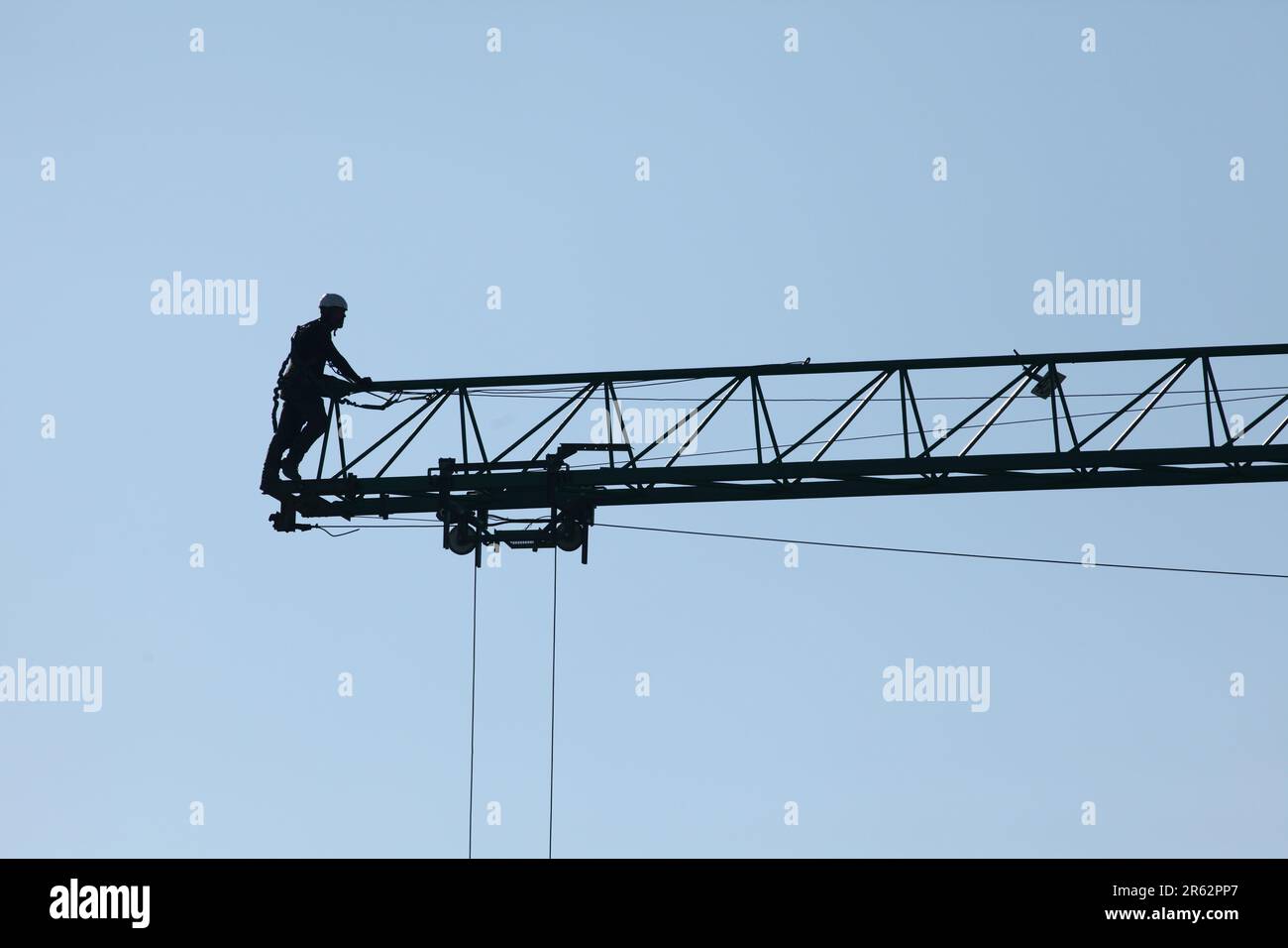 Un uomo che indossa un'attrezzatura di sicurezza è fissato saldamente a una gru collegata a una linea elettrica tramite funi spesse Foto Stock