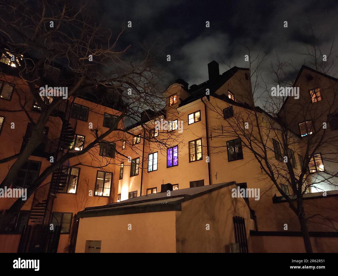Una vista notturna scura di un edificio moderno, illuminato da diverse finestre e illuminato sullo sfondo di un cielo notturno pieno di stelle Foto Stock