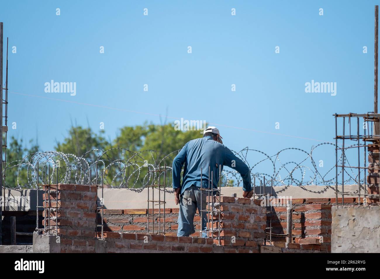 Un lavoratore di costruzione che indossa un elmetto e giubbotto di sicurezza è visto attentamente costruire un muro di mattoni con una cazzuola Foto Stock