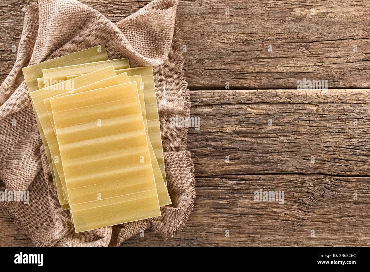 Sfoglia di lasagne rigate a secco, non cotte, fotografata in alto su legno rustico con copia di lato Foto Stock