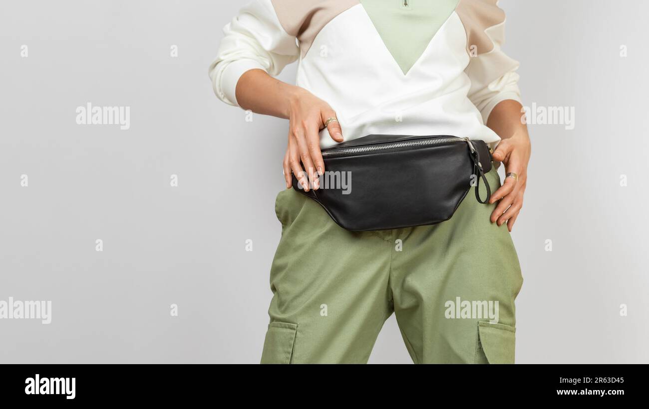 Borsa a banana in pelle nera per donna con pantaloni verdi e spazzatura su sfondo grigio con Copy Space Foto Stock