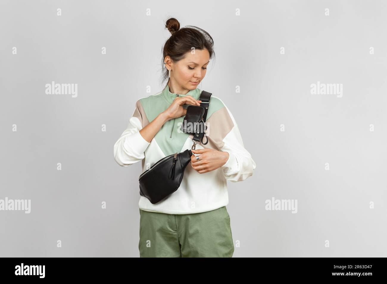Donna che indossa una borsa in pelle nera in vita con un accessorio portamonete rimovibile per riporre chiavi, sigaretta o auricolari attaccati alla tracolla, Studio Shot Foto Stock