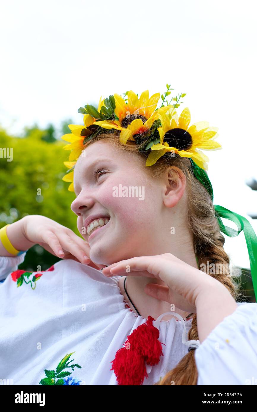 Una bella ragazza dai capelli rossi raddrizza la sua treccia sulla sua testa una corona di girasoli una camicia Ucraina ricamata un sorriso luminoso denti bianchi sullo sfondo di una primavera verde Foto Stock