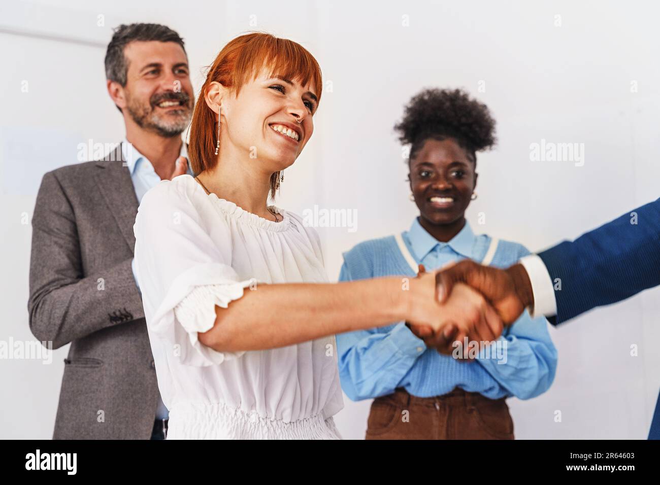 Una donna caucasica guarda la fotocamera mentre scuote le mani con un uomo africano in un ufficio professionale. Supporto per colleghi di diversa provenienza Foto Stock