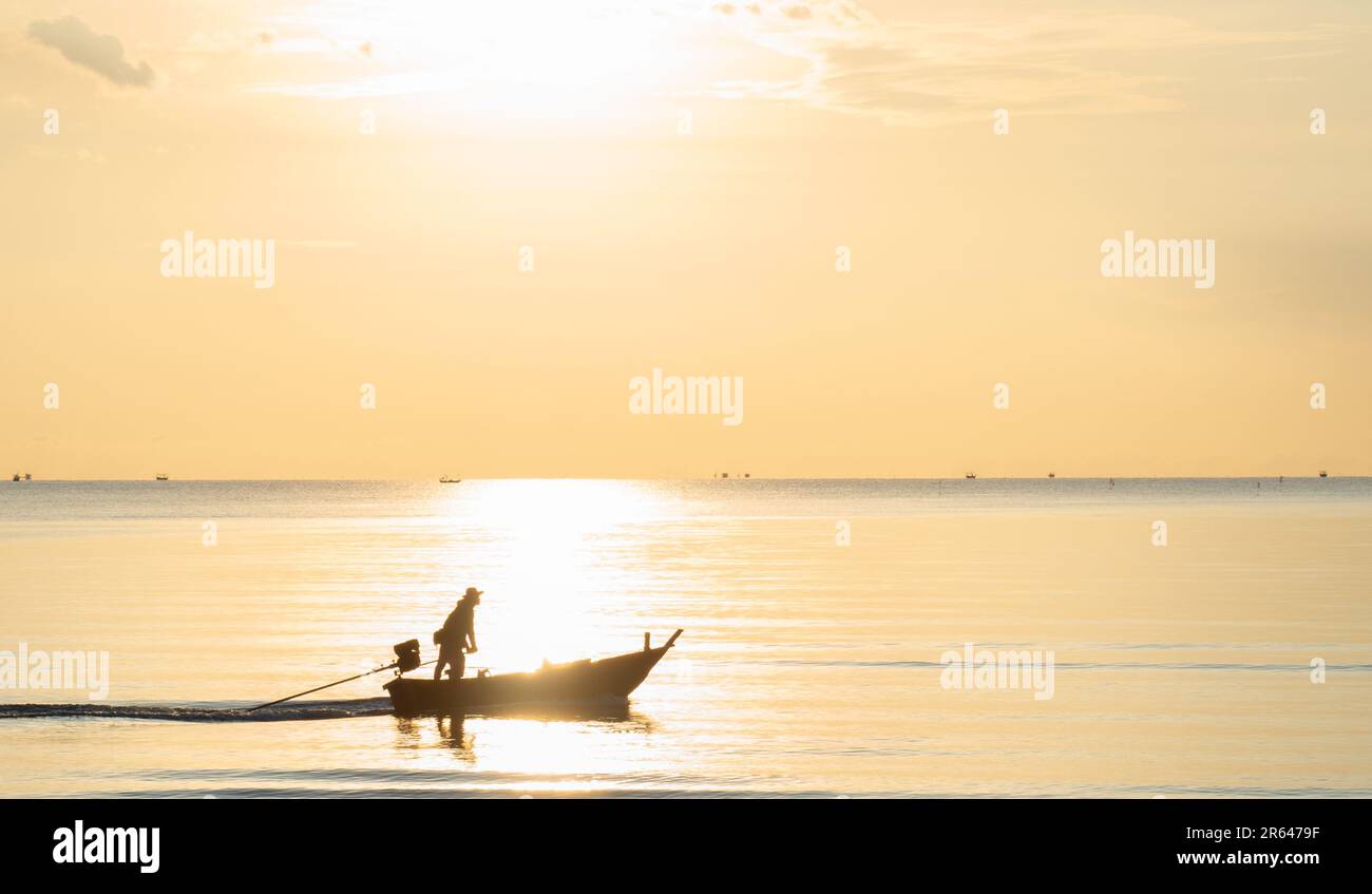 Pescatore silhouette che naviga verso il mare la mattina presto. Mare e cielo brillano di raggio d'oro, atmosfera tranquilla e tranquilla. Foto Stock