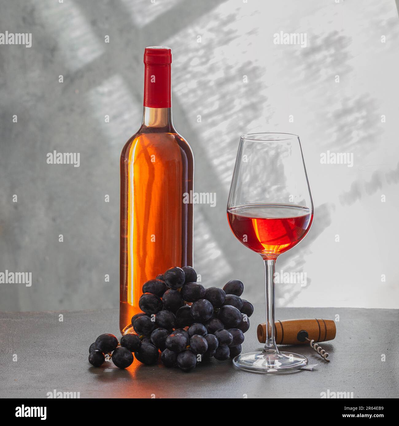 Bottiglia di vino rosato, bicchiere di vino e uva su fondo grigio in cemento. Concetto di vinificazione e degustazione del vino. Foto Stock