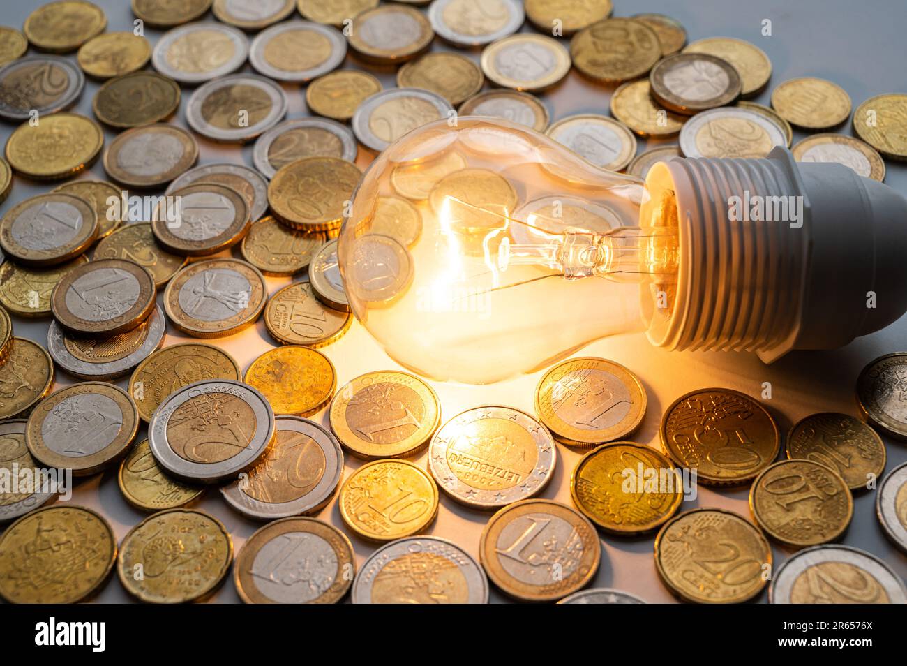 Lampadina accesa, con monete intorno. Aumento delle tariffe per l'elettricità, della dipendenza energetica, delle fonti energetiche e dell'approvvigionamento energetico. Foto Stock