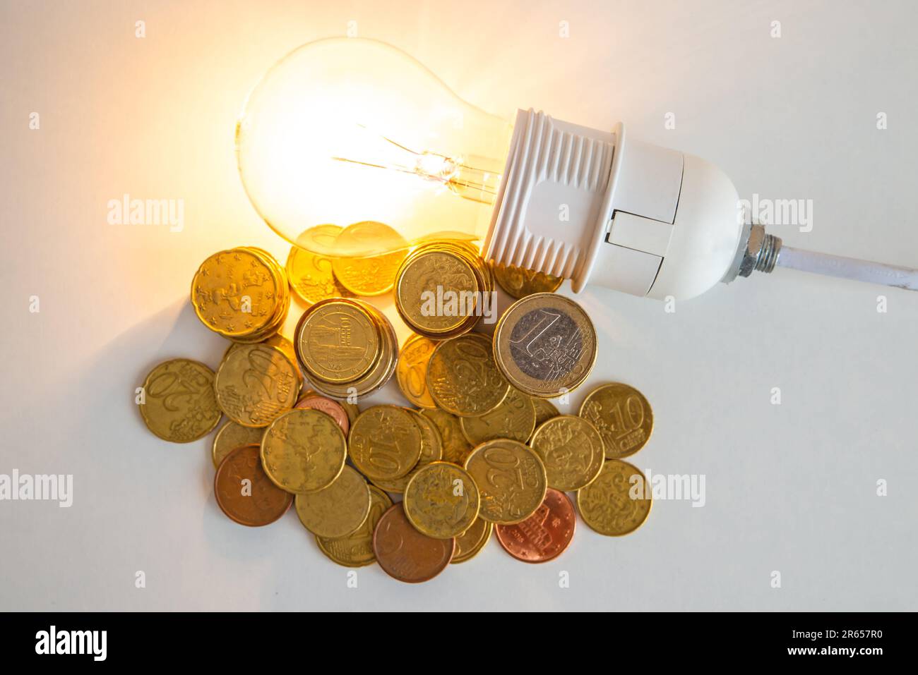 Lampadina accesa, con monete accanto ad essa. Aumento delle tariffe per l'elettricità, dipendenza energetica, fonti di energia e forniture di energia. Foto Stock