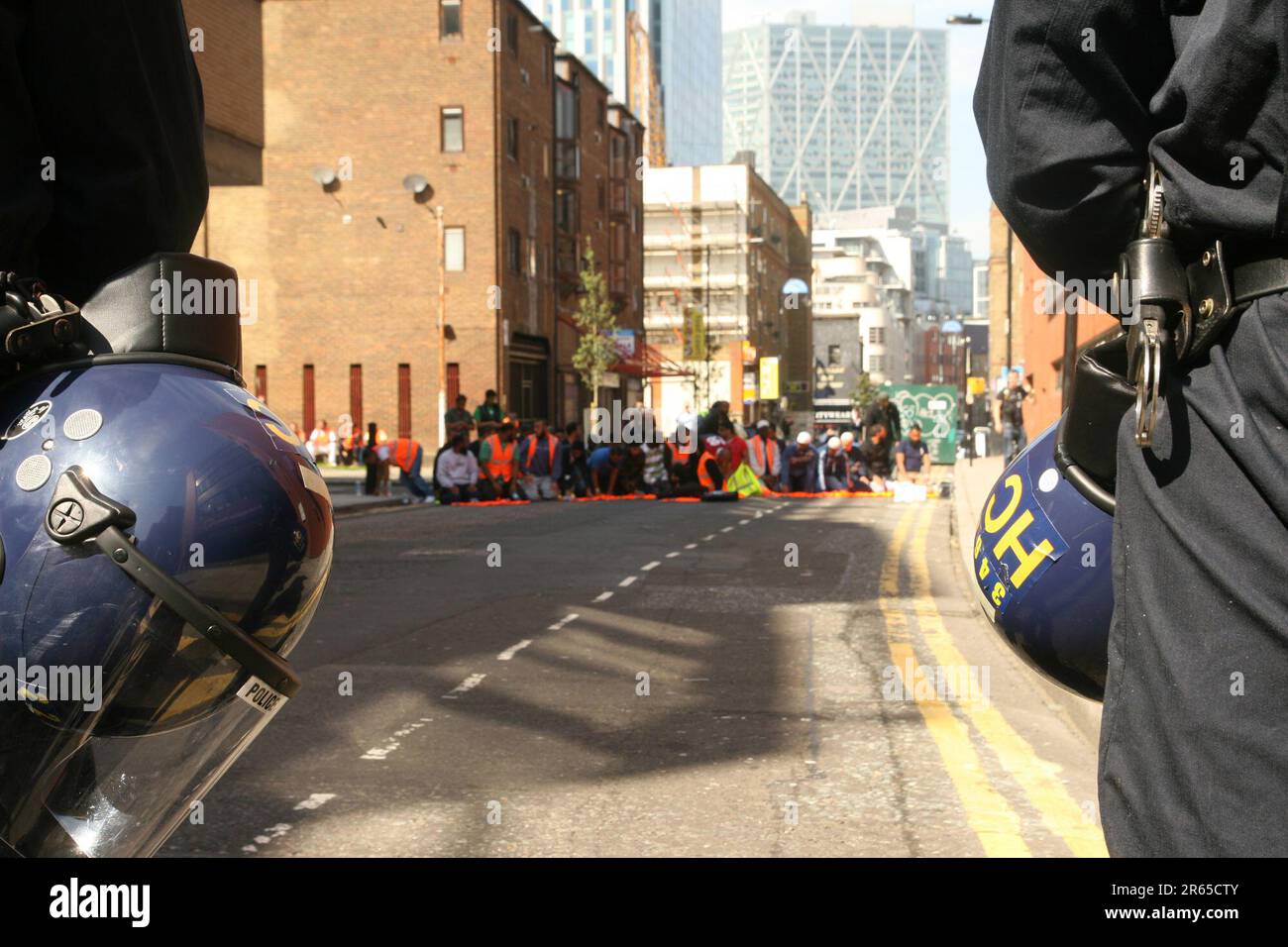 La polizia controlla gli steward musulmani che si accingono a pregare a Whitechapel mentre gli estremisti di destra della Lega della Difesa inglese (EDL) si trovano di fronte a Tower Hamlets di Londra Foto Stock