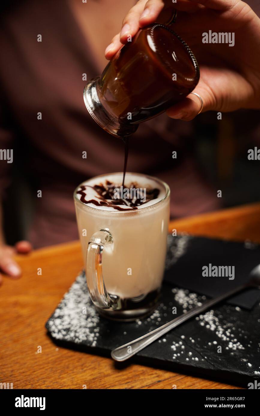 Primo piano della giovane donna caucasica in abbigliamento casual versando sciroppo in bevanda sul piatto Foto Stock