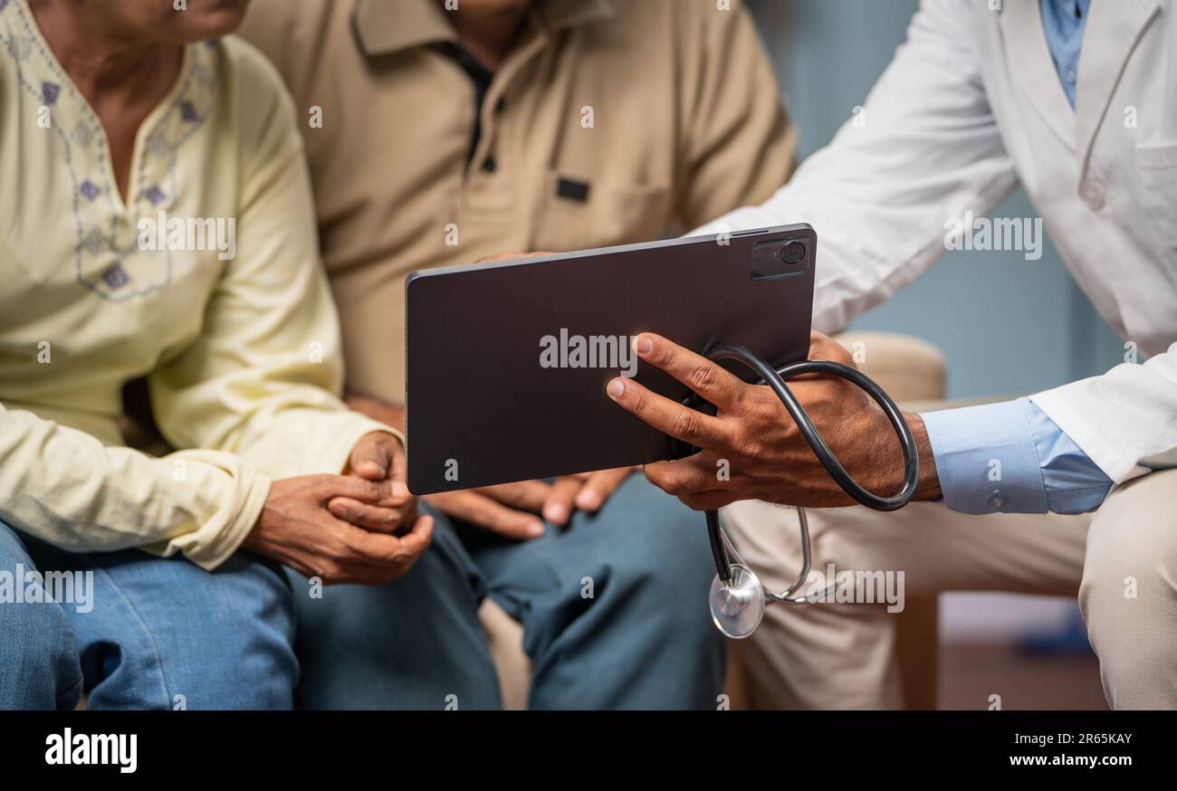 Primo piano del medico indiano che mostra rapporto medico a coppia senior su tablet digitale a casa - concetto di tecnologia, trattamento e consultazione. Foto Stock