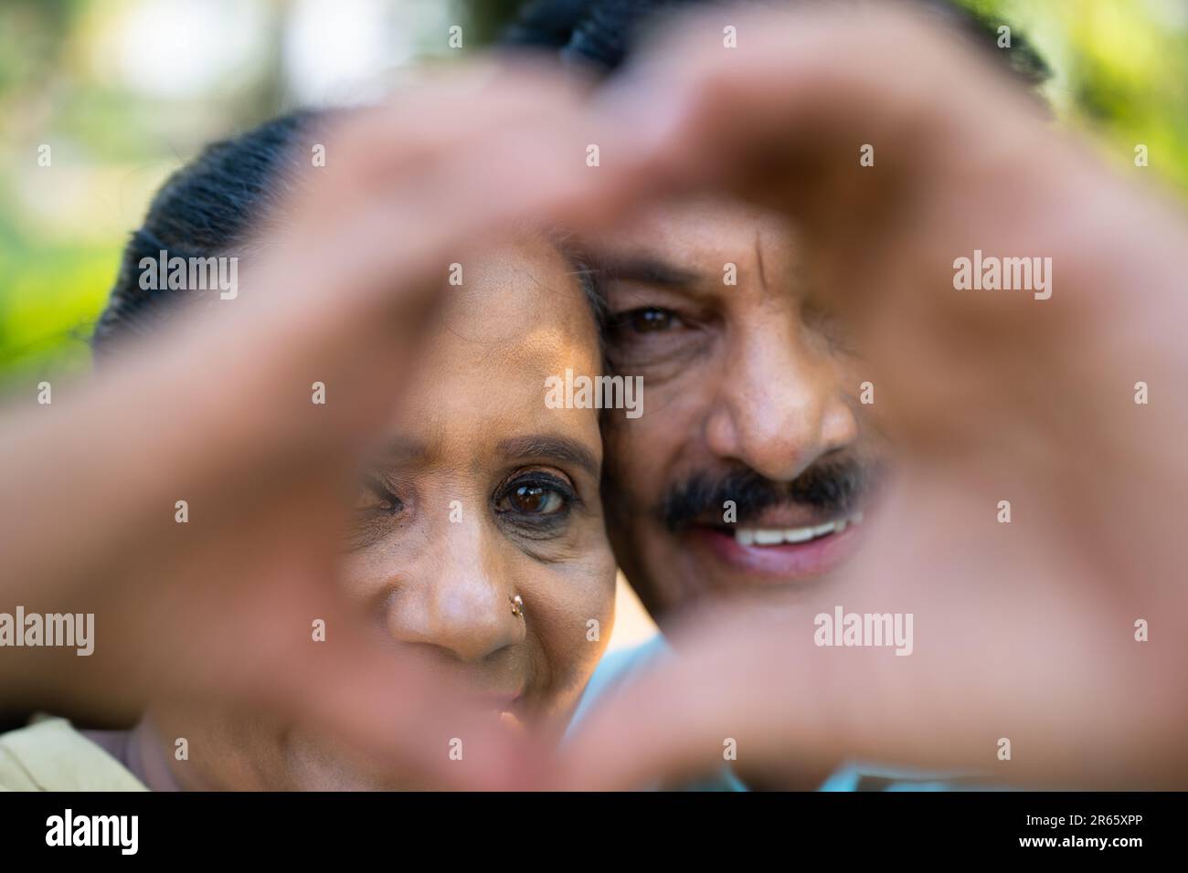 Indiano felice anziano coppia che mostra segno o gesto di cuore guardando la macchina fotografica - concetto di amore, affetto e legame di lunga relazione Foto Stock