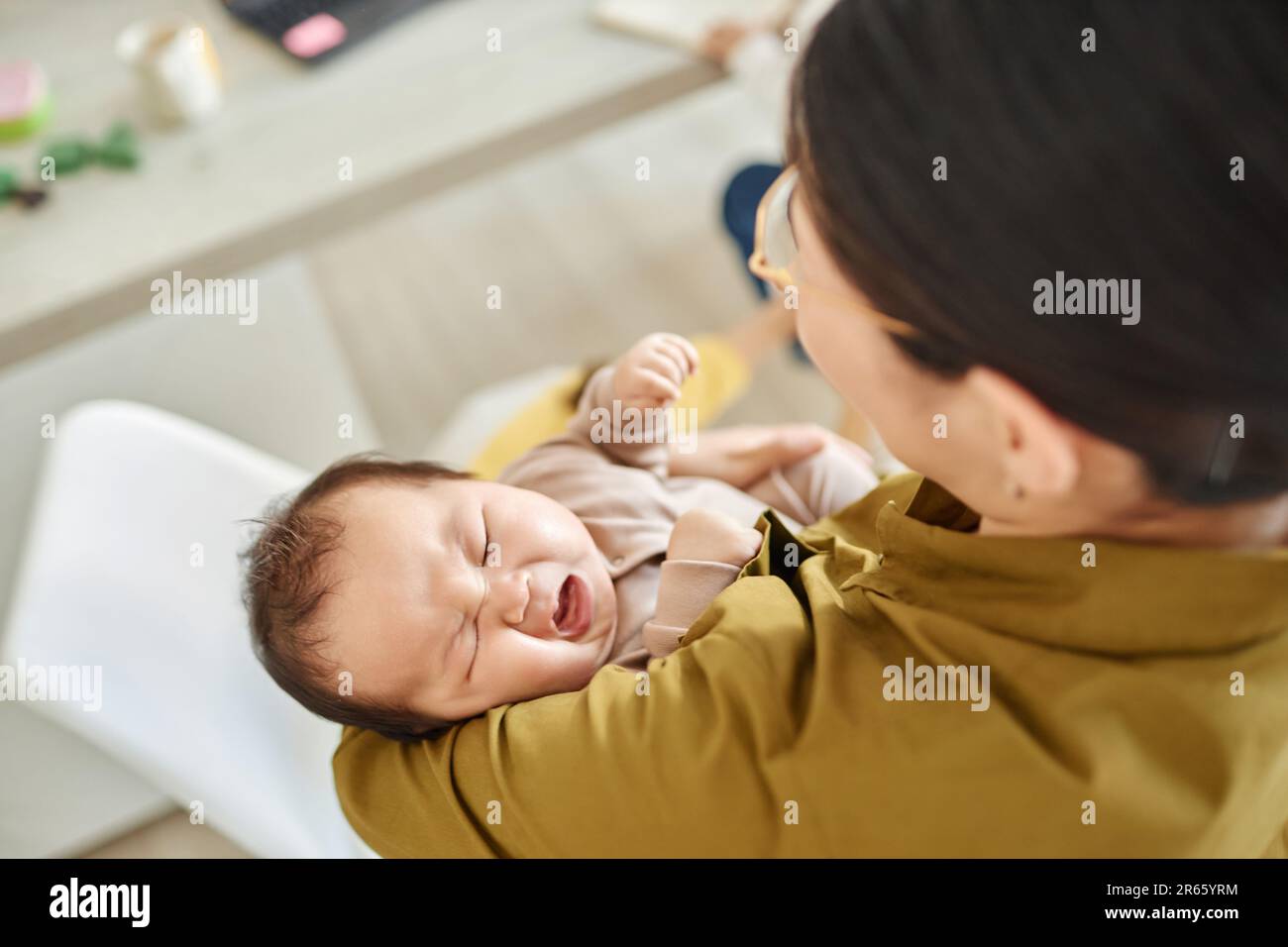 Vista posteriore della giovane mamma che tiene il suo bambino sulle braccia e lulling lui a dormire Foto Stock