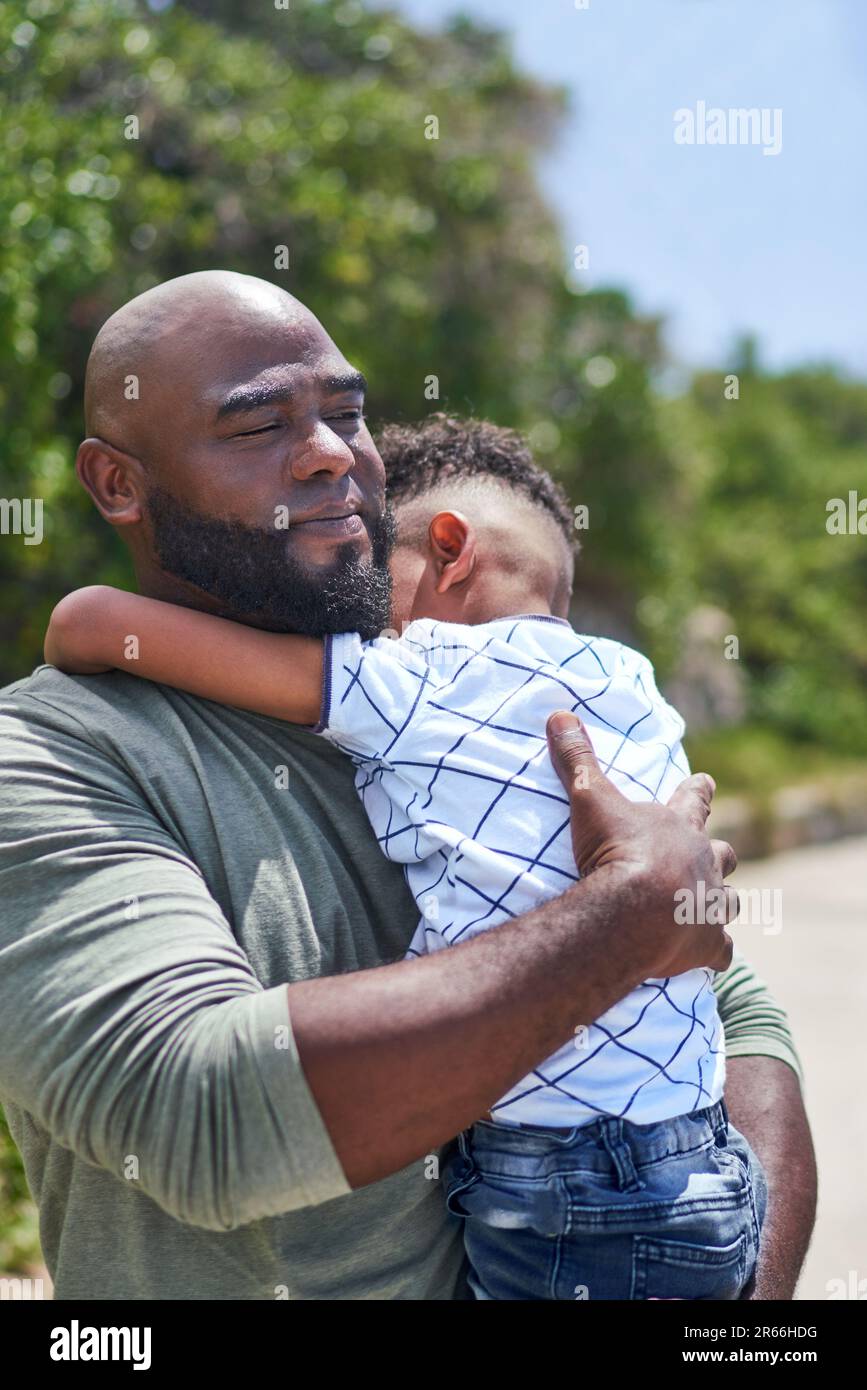 Padre affettuoso che tiene il figlio stanco sul sentiero soleggiato Foto Stock