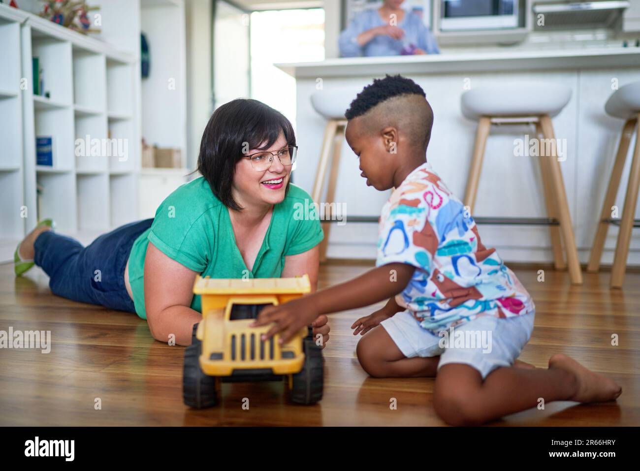 Madre e figlio felici che giocano con il camion giocattolo a terra a casa Foto Stock