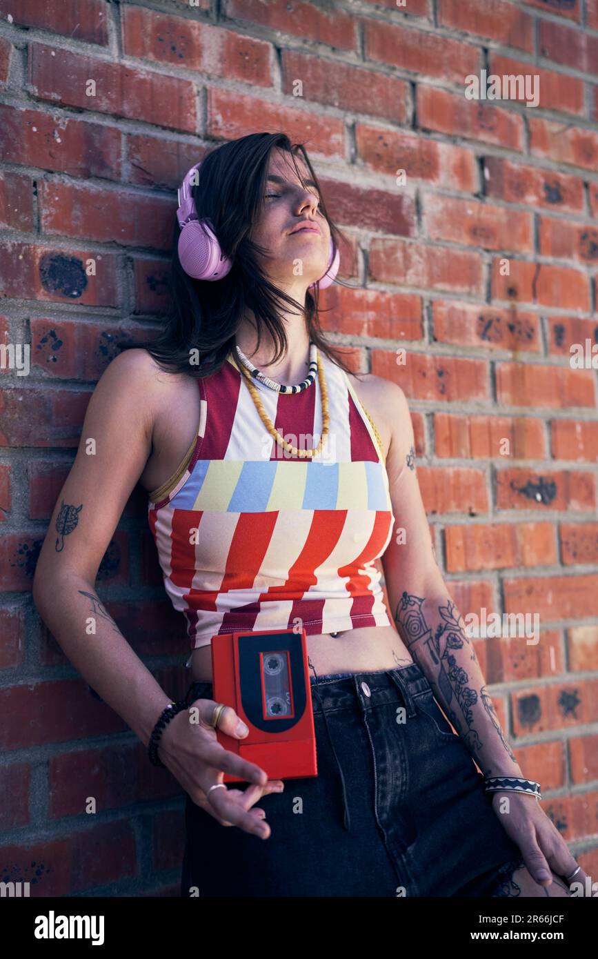 Giovane donna fresca con tatuaggi che ascoltano musica con le cuffie Foto Stock