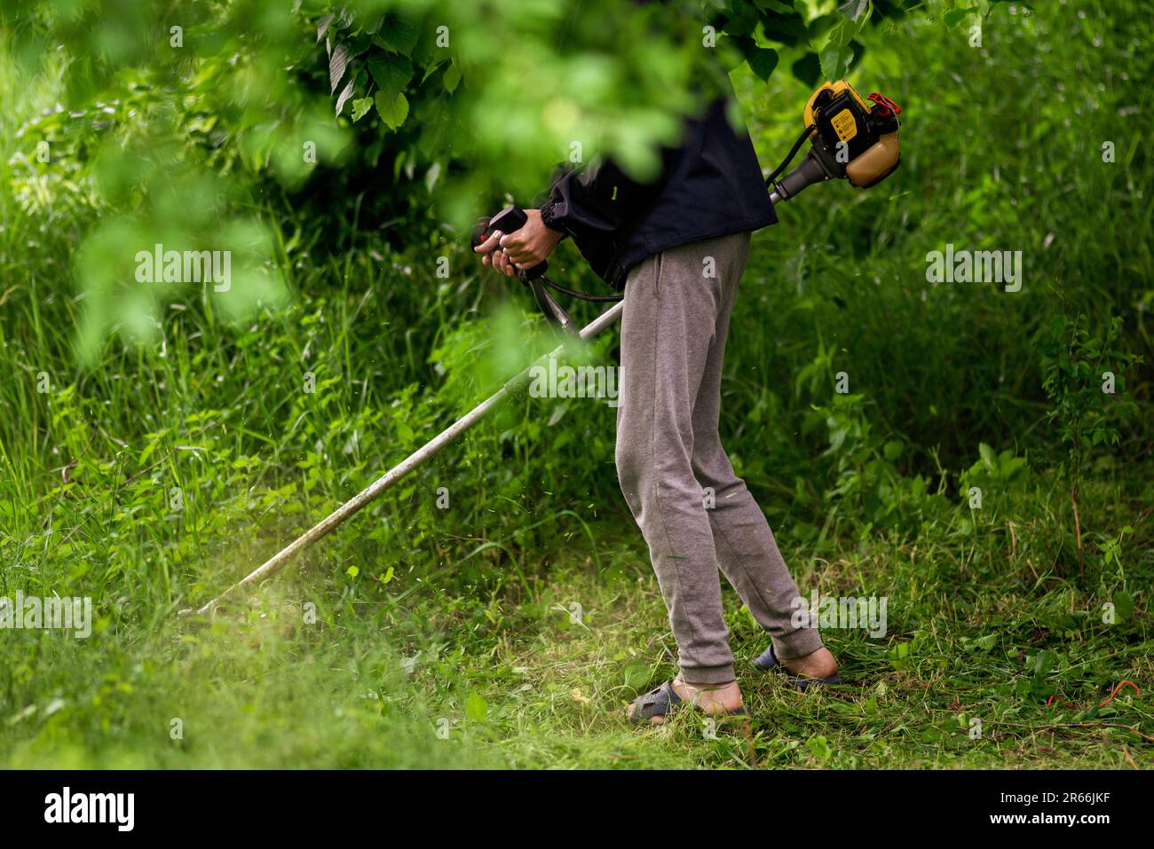 Uomo da lavoro giardiniere caucasico tagliaerba manuale tagliaerba tagliaerba a mano tagliaerba o pinzetta elettrica o taglierina a spazzola Prato Mace Gasoline primo piano Foto Stock