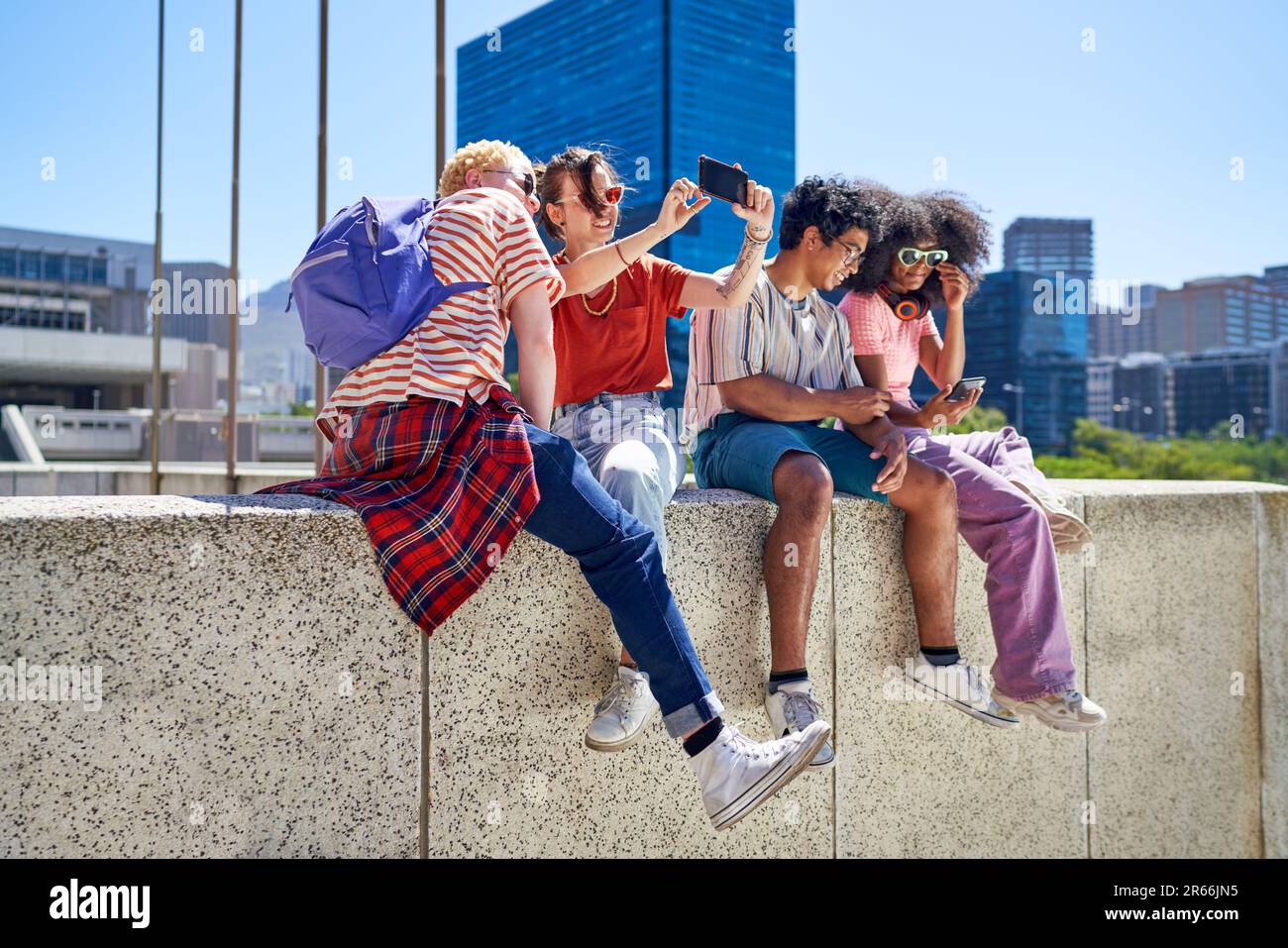 Giovani amici che si aggrappano, utilizzando gli smartphone in città soleggiata Foto Stock