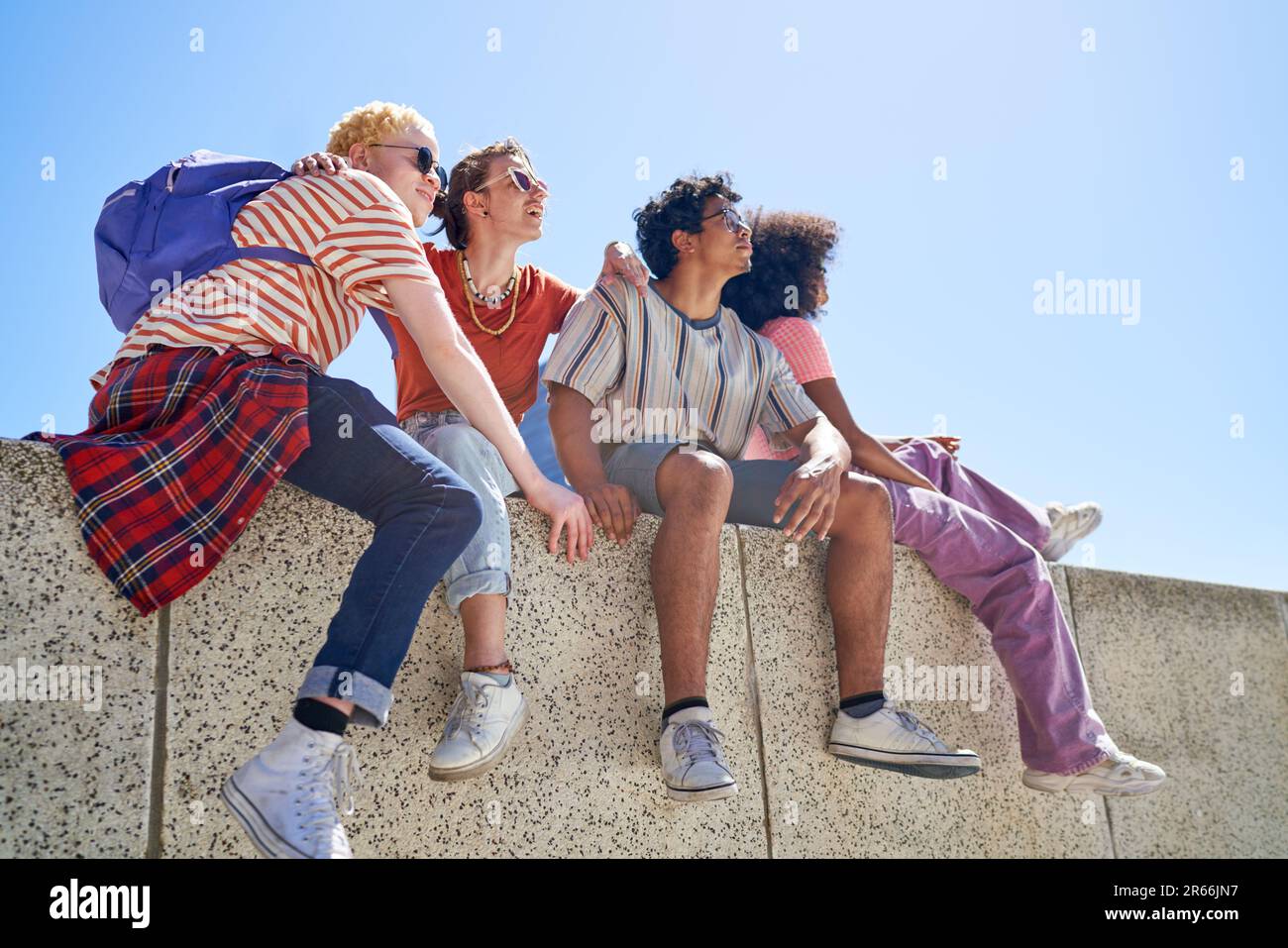 Giovani amici di coppia che si appendono fuori, seduti su una sporgenza soleggiata Foto Stock