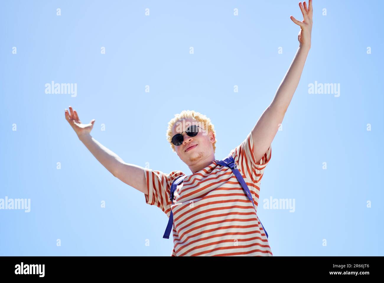 Ritratto fresco giovane uomo con le braccia sollevate sotto il cielo azzurro soleggiato Foto Stock