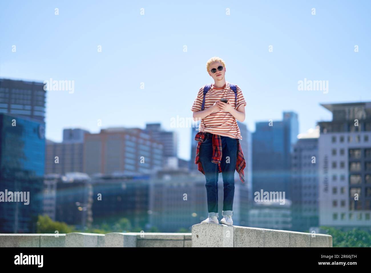 Ritratto giovane uomo con smartphone sulla sporgenza in città soleggiata Foto Stock