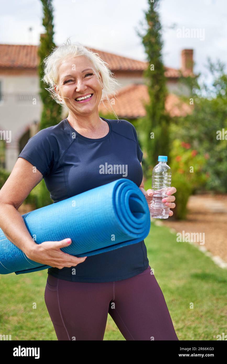 Ritratto felice donna anziana con materassino yoga in giardino estivo Foto Stock