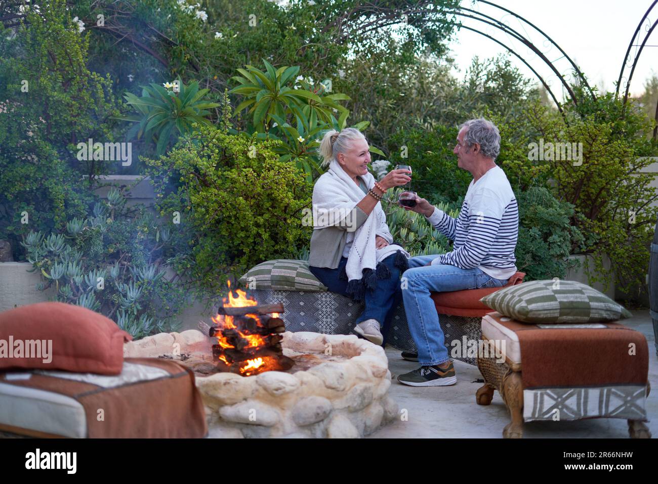 Felice coppia anziana bere vino presso la buca del fuoco sul patio giardino Foto Stock