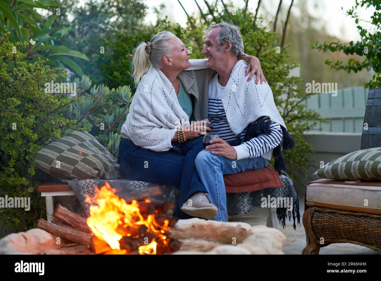 Felice coppia anziana bere vino e abbracciando dalla buca del fuoco sul patio Foto Stock