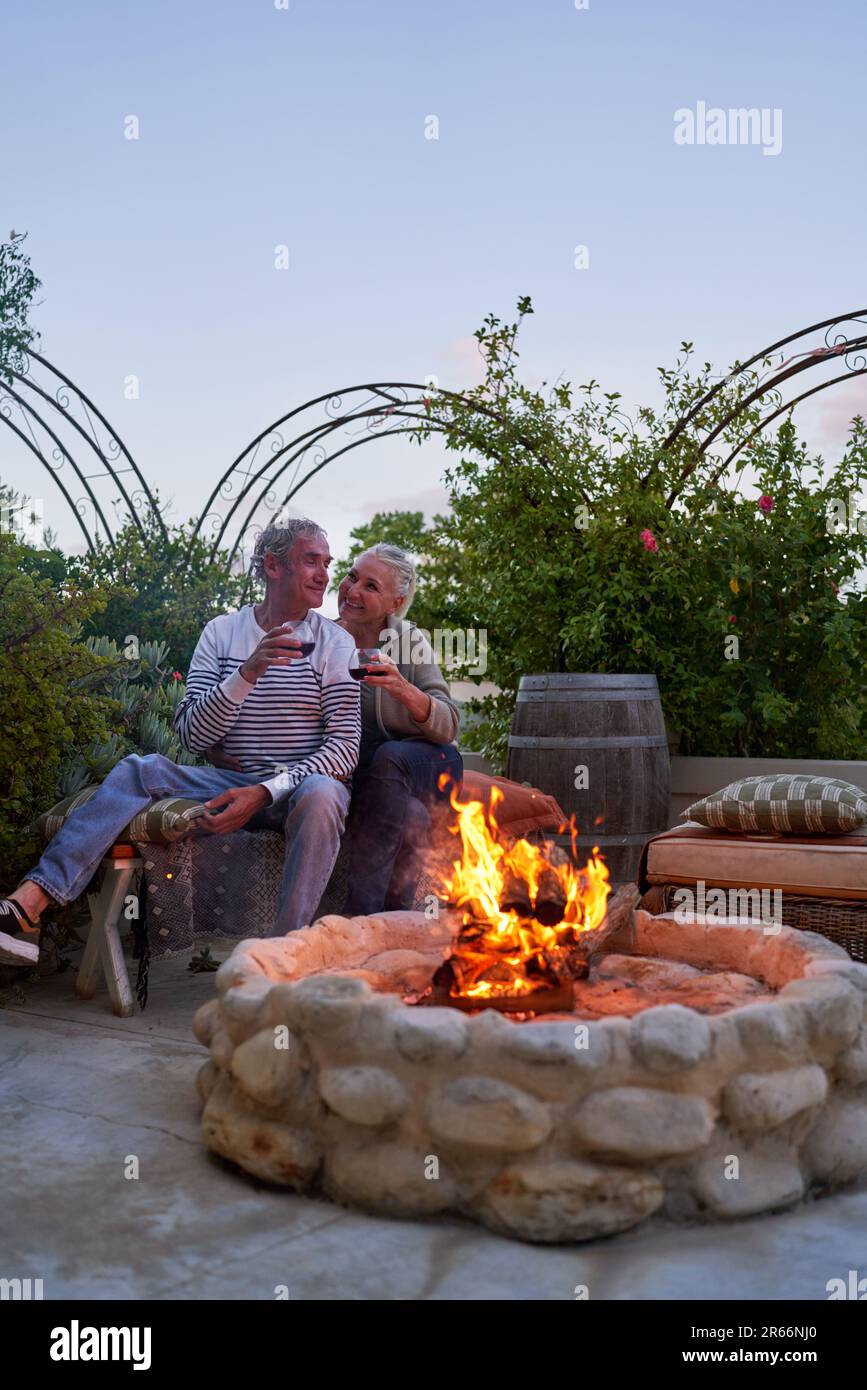 Felice coppia anziana bere vino presso la fossa del fuoco sul patio estivo Foto Stock