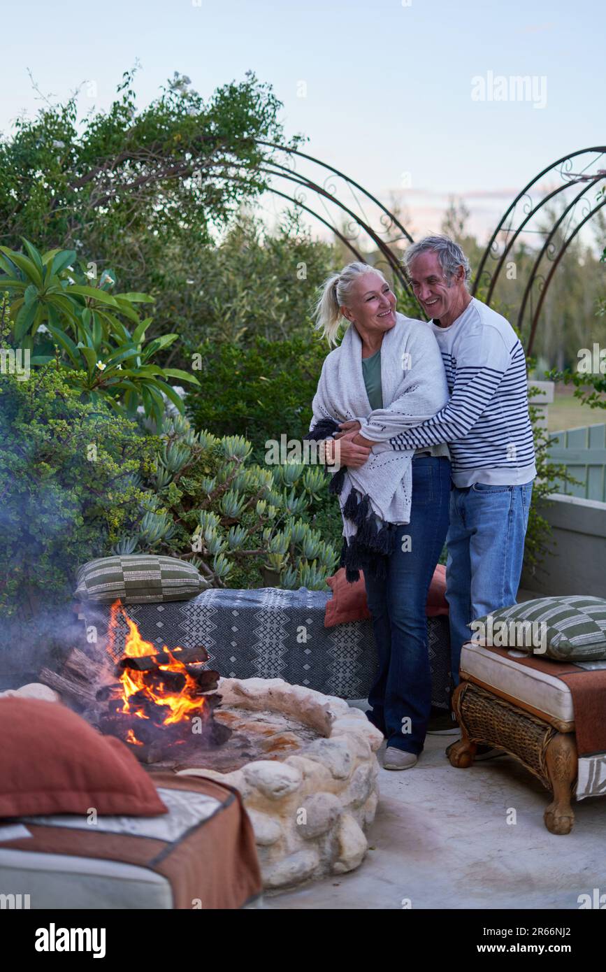 Coppia anziana felice abbracciando dalla buca del fuoco sul patio del giardino Foto Stock