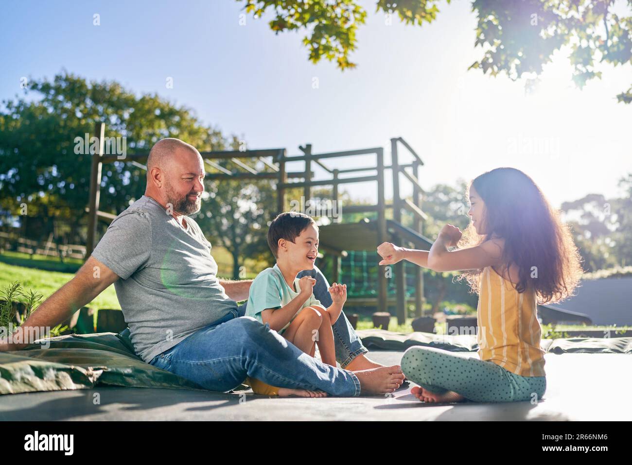 Padre e bambini seduti sul trampolino nel soleggiato cortile Foto Stock