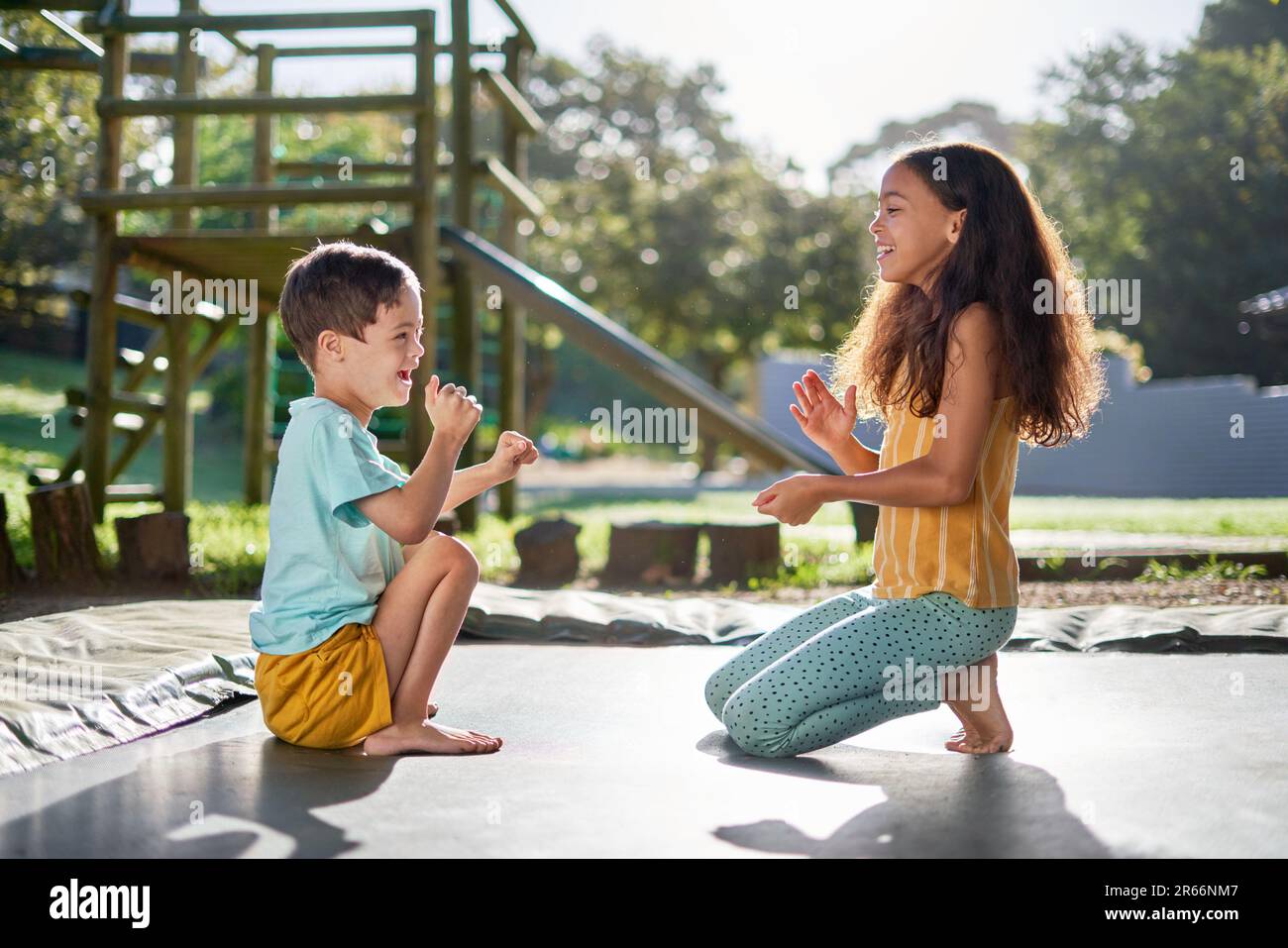Felice fratello e sorella giocando gioco di battimento sul trampolino soleggiato Foto Stock