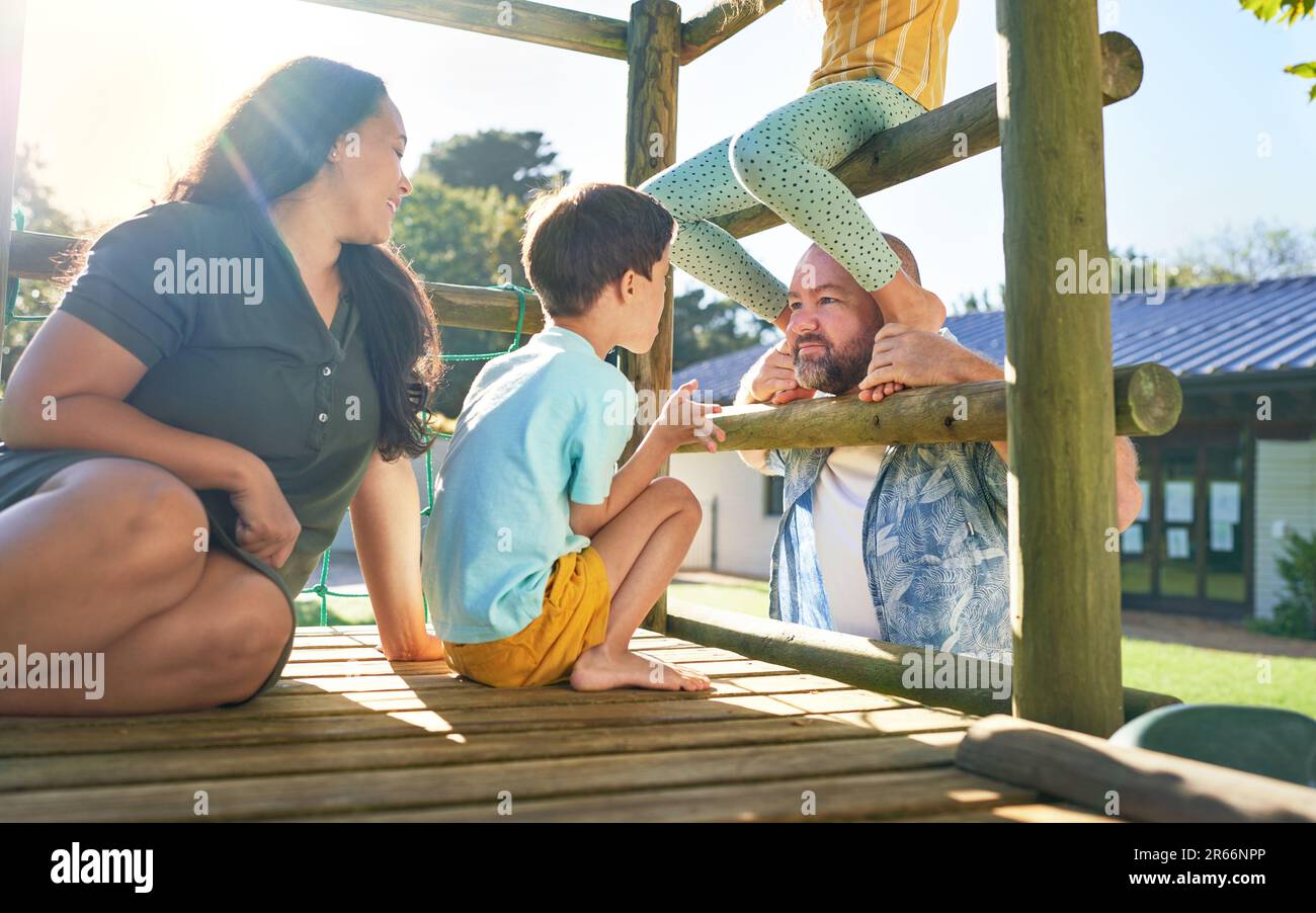 Felice famiglia che gioca al parco giochi struttura in un parco soleggiato Foto Stock