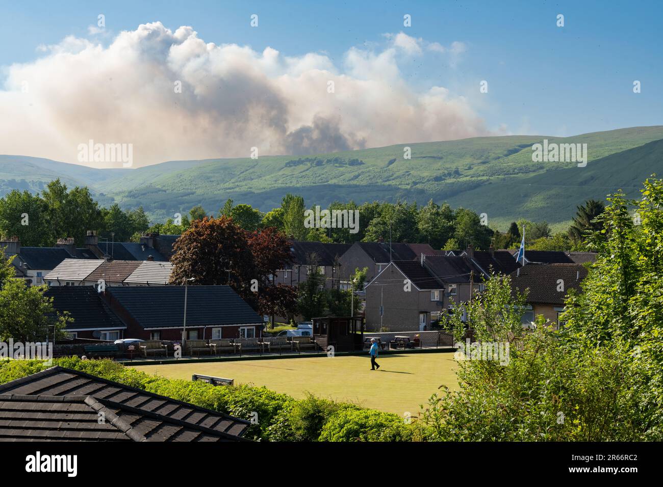 Lennoxtown, East Dunbartonshire, Scozia, Regno Unito. 7th giugno, 2023. Il servizio antincendio e di soccorso scozzese ha lanciato un avvertimento in tutta la Scozia riguardo a un rischio di incendio selvaggio "molto elevato". Nella foto: Nuvole di fumo da un fuoco selvatico che brucia sui campsie Fells come visto dalla città di Lennoxtown nel tardo pomeriggio come un gioco di bocce è in corso al Campsie Bowling Club Credit: Kay Roxby/Alamy Live News Foto Stock