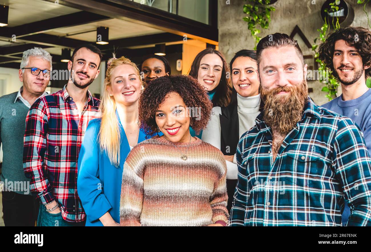 I lavoratori multigenerazionali e multietnici sorridono davanti alla telecamera all'interno di un ufficio d'affari modico - multiculturale, impiegati di lavoro, imprenditore e te Foto Stock