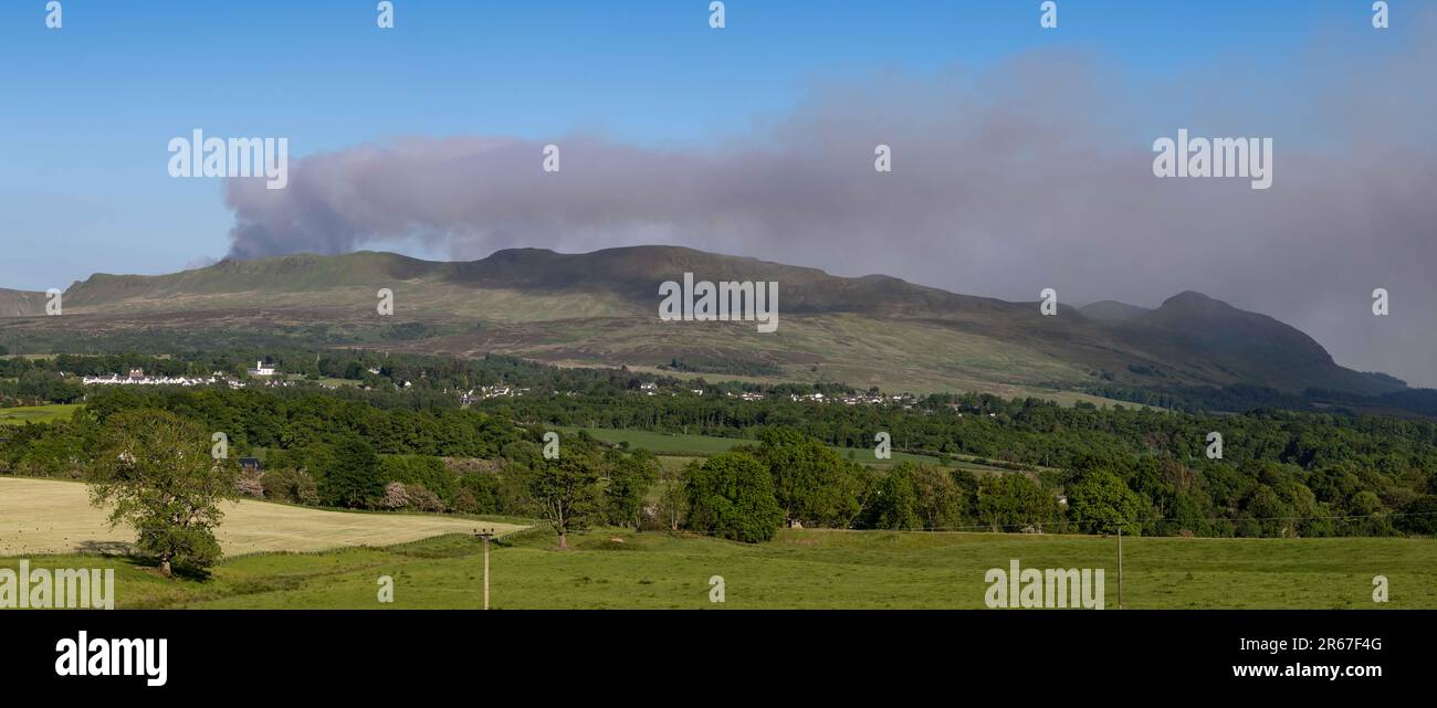 Killearn, Stirling, Scozia, Regno Unito. 7th giugno, 2023. Il servizio antincendio e di soccorso scozzese ha lanciato un avvertimento in tutta la Scozia riguardo a un rischio di incendio selvaggio "molto elevato". Nella foto: Nuvole di fumo da un fuoco selvatico che brucia sulle campsie Fells come visto sopra il villaggio di Killearn nel tardo pomeriggio. Scottish Fire and Rescue ha affermato che "a causa di un bombardamento in elicottero, consigliamo ai residenti locali di evitare l'area e di tenere chiuse le finestre e le porte". Credit: Kay Roxby/Alamy Live News Foto Stock