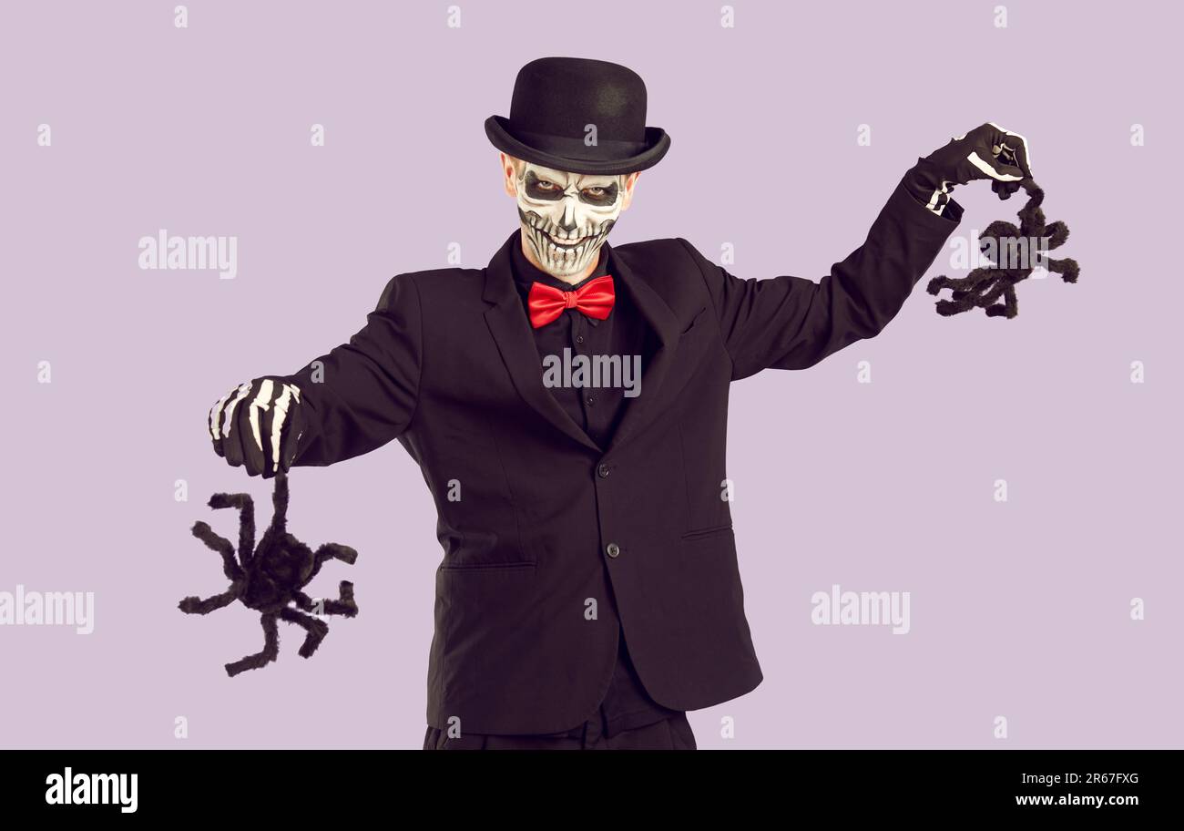 Uomo in Halloween vestito con sorriso minaccioso spaventa con due ragni decorativi. Foto Stock