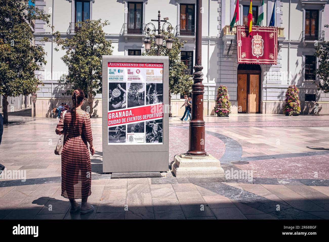 Ragazza che guarda un poster di eventi sportivi per le strade di Granada. Foto Stock
