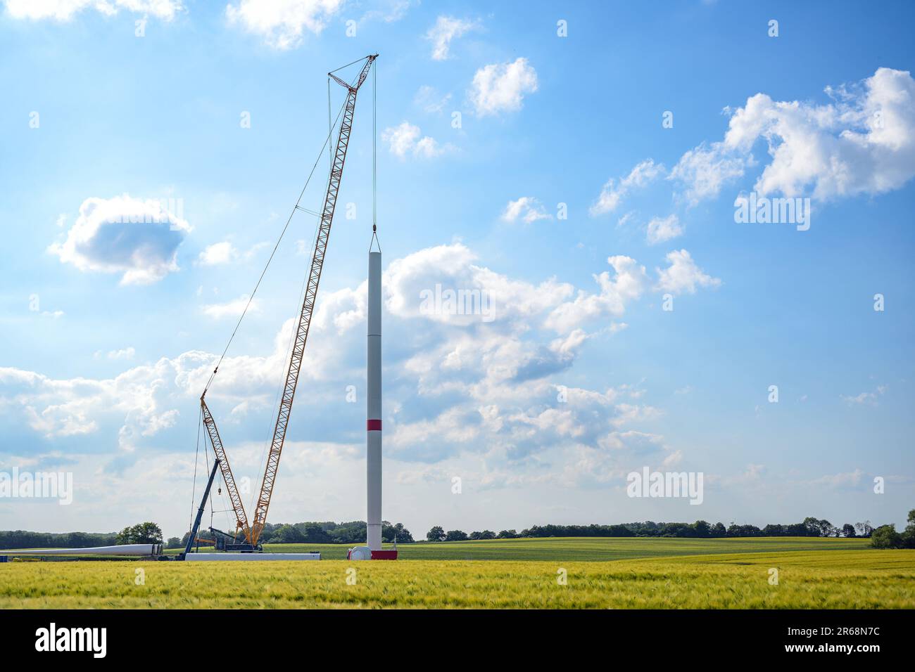 Cantiere di una turbina eolica, gru alta che installa un tubo sulla torre, navicella, mozzo del rotore e pale giacenti ancora sul terreno, ene rinnovabile Foto Stock